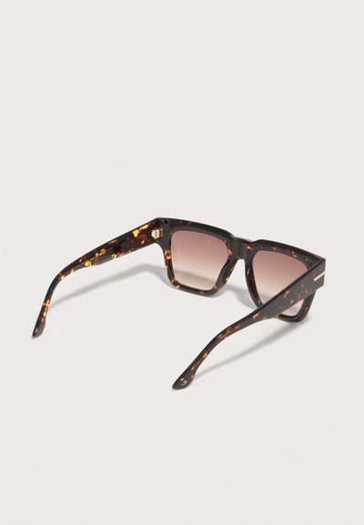 Γυαλιά ηλίου με τετράγωνους σκελετούς σε σχέδιο χελώνας και βαθμιαία καφέ φακούς, ανοιχτά πάνω σε ένα ανοιχτόχρωμο υπόβαθρο.