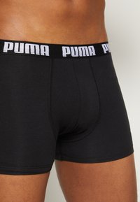 Black cotton boxer briefs with a wide elastic waistband featuring white "PUMA" branding. Smooth fabric, fitted design, and mid-length cut.