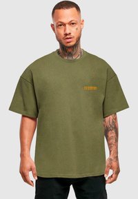 Oliven Grøn oversized t-shirt lavet af bomuld, med korte ærmer og et lille orange logo på brystet. Simpelt, udekoreret design.