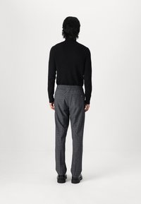 Un col roulé noir côtelé associé à un pantalon à carreaux gris avec une taille élastique. Le modèle se tient de dos, portant des chaussures noires.