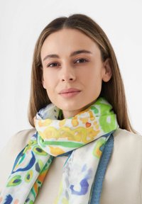 Écharpe légère multicolore présentant des motifs abstraits en vert, jaune et bleu, confectionnée dans un tissu doux et texturé avec des bords contrastés.