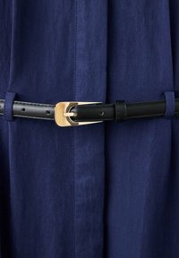 Ceinture en cuir noir avec une boucle dorée attachée autour d’un tissu bleu marine avec des passants de ceinture.