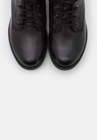 Schwarze Lederstiefel mit abgerundeten Zehen, ausgestattet mit einem Schnürdesign und profilierten Sohlen. Nähte entlang der Seitennähte sind sichtbar.