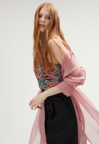 Top corto colorido y texturizado con piezas de tela en capas en rosa, verde y azul, combinado con una falda de satén negra y un overlay transparente rosa.