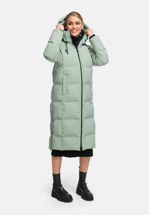 Giacca a vento verde chiaro con zip sul davanti, cappuccio regolabile, tasche laterali e silhouette lunga, abbinata a stivali neri chunky.