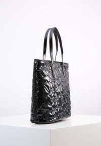 Czarna torba na ramię z błyszczącym, pikowanym wzorem, podwójnymi płaskimi uchwytami oraz srebrnym akcentem z logo. Wykonana z błyszczącego materiału syntetycznego.