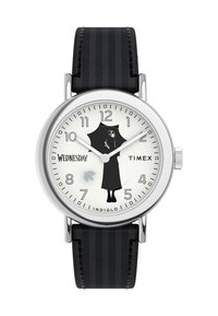 Timex kell, millel on hõbedane roostevabast terasest korpus, valge kellalace, must siluett, musta triibuline nahkrihm ja "Indiglo" funktsioon.