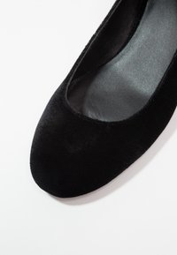 Ballerine plate en velours noir avec un bout arrondi et lisse et une légère brillance. Elle possède une doublure intérieure douce et un petit talon pour le confort.
