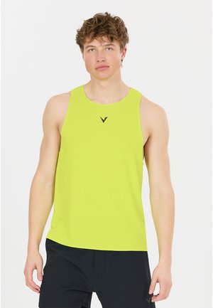 Ung mand med kort krøllet hår iført en klart gul ærmeløs sportstrøje og sorte shorts mod en ensfarvet hvid baggrund.