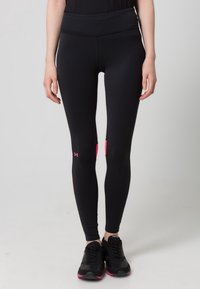 Donna che indossa leggings neri a vita alta con dettagli rosa e scarpe da ginnastica nere, in piedi su uno sfondo neutro.