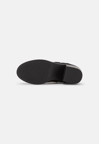 Semelle de chaussure noire avec une surface texturée, présentant un orteil arrondi et un talon plat. Le matériau semble en caoutchouc avec une finition mate et propre.