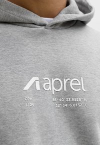 Približnji posnetek sive kapucarice z belo oznako »aprel« in geografskimi koordinatami, natisnjenimi na prsnem predelu.