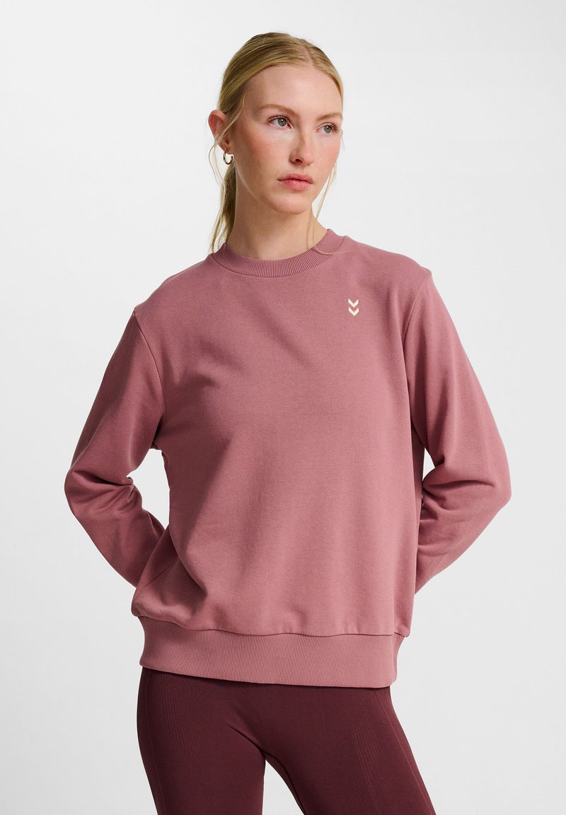 Lyserød sweatshirt med lange ærmer, ribbet halsudskæring og kant. Har et diskret logo på brystet. Glat tekstur, afslappet pasform.