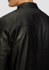 Zwarte leren jas met een gladde textuur, minimale stikdetails, een kleine kraag en een recht gesneden achterkant.