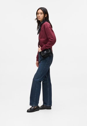 Maroon sweatshirt with a high collar, dark blue wide-leg jeans, black studded loafers, and a black crossbody bag with a logo.