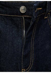 Mørkeblå denim jeans med en metalknap, lynlåsåbning og kontrasterende gule syninger langs sømmene og lommerne. Glat tekstur.