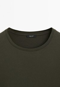 Dunkelolivgrünes T-Shirt mit Rundhalsausschnitt und einem schwarzen Etikett mit der Aufschrift "Massimo Dutti Made in China" im Kragen.