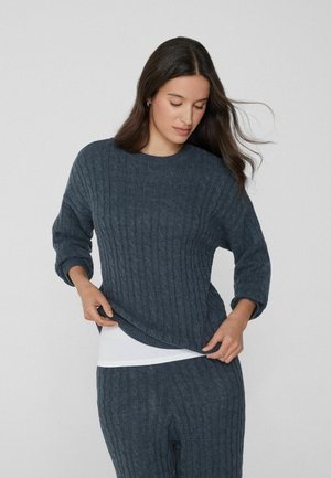 Granatowy sweter z dzianiny o prążkowanej fakturze, z okrągłym dekoltem i rękawami 3/4, zestawiony z białą warstwą pod spodem.