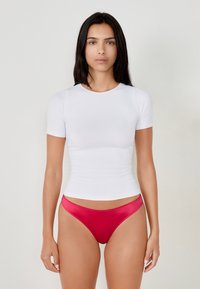 Top bianco aderente a maniche corte abbinato a perizoma in satin rosso. Tessuto liscio, scollatura rotonda e leggera arricciatura in vita.