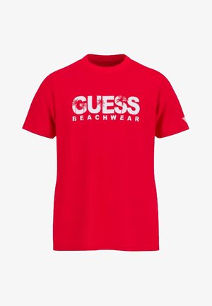 T-shirt rouge à manches courtes avec texte blanc "GUESS BEACHWEAR" et graphismes de palmiers sur le devant, col rond.