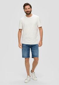 Biała bawełniana koszulka, niebieskie szorty dżinsowe i białe sneakersy z czarnymi akcentami. Krótkie rękawy, podwinięte nogawki szortów, casualowy krój.