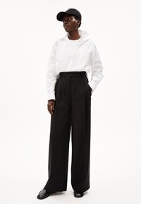Witte blouse met opgevouwen kraag, zwarte high-waisted wijde broek en zwarte pet. Glad materiaal en op maat gemaakte ontwerp.