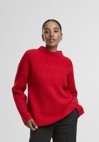 Czerwony sweter z dzianiny o strukturalnej fakturze i wysokim kołnierzu, z długimi rękawami i lekko luźnym krojem. Akcenty z kontrastowymi krawędziami.