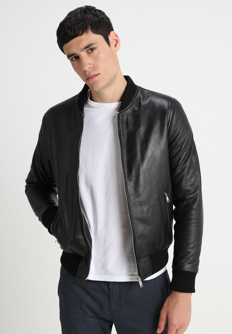 Zwarte leren bomberjack met ribgebreide manchetten en kraag, met een ritsluiting en zijzak. Gedragen over een wit T-shirt.