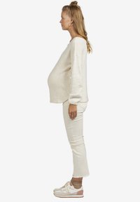 Hellbeige gestrickter Pullover mit Puffärmeln, kombiniert mit weißen, schmal zulaufenden Jeans und weißen Sneakers mit rosa Akzenten.