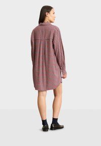 Robe chemise à carreaux rouges et bleus avec des manches longues, des poignets boutonnés, un col et une coupe décontractée. Détail de plis au dos pour plus de volume.