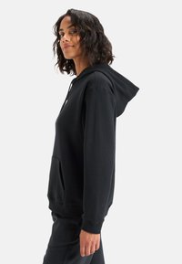 Sudadera con capucha negra hecha de una tela suave, que cuenta con un bolsillo frontal, capucha ajustable con cordón y puños y dobladillo acanalados.