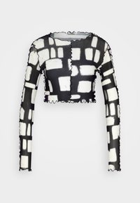 Svart och vit beskuren långärmad topp med rutmönster, med volangkanter och ett transparent, lätt tyg.