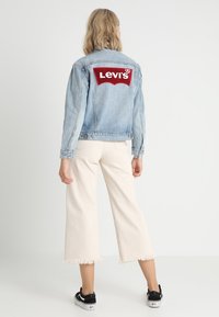 Světle modrá džínová bunda s velkou červenou nášivkou s logem „Levi's“ na zádech. Kombinováno s bílými zkrácenými kalhotami a černými teniskami.
