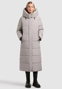 Cappotto imbottito lungo di un grigio chiaro con colletto alto, due tasche laterali e una texture liscia, abbinato a stivali con zeppa neri.