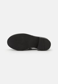 Semelle d'une chaussure habillée noire avec une texture lisse, un bout arrondi et un talon légèrement surélevé sur un fond gris clair.