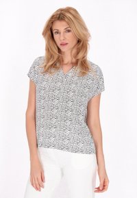 Kortsleeve blus i svart och vitt med mönster av blommor, design med V-ringning, avslappnad passform och mjuk kvalitet. Matchas med vita byxor.