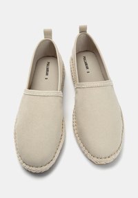 Beige kanvas slip-on sko med en tekstureret overdel, elastiske sidepaneler og vævet jute-detaljering langs sålen. Model: Pull&Bear.
