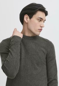 Pulover tricotat de culoare verde închis, cu guler rotund și mâneci lungi, având o textură moale și manșete striate pentru un ajustaj îmbunătățit.