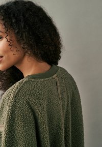 Grøn fleece sweater med en tekstureret overflade, ribbet krave og kontrastsyninger langs sømmene. Let løstsiddende pasform, afslappet design.