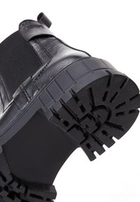 Stivale in pelle nera con suola in gomma spessa, caratterizzato da un motivo di battistrada testurizzato per una migliore aderenza e un pannello laterale elastico per una facile calzata.