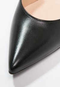 Gros plan sur une chaussure en cuir noir à bout pointu, finition lisse et brillante, avec une doublure intérieure beige.