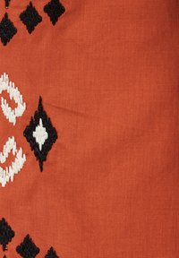 Tekstila audums ar oranžu pamatu un baltām un melnām izšūtām dimantu un lapu rakstiem. Gluda tekstūra, izturīga konstrukcija.
