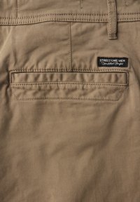 Beige puuvillashortsit sileällä pinnalla, joissa on takatasku ja musta etiketti, jossa lukee "STREET ONE MEN" vyötäröllä.