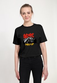 Czarna bawełniana koszulka z wyrazistym nadrukiem graficznym, na którym znajduje się napis "AC/DC" na czerwono oraz "PWR UP" na żółto, a także monochromatyczny obraz zespołu.
