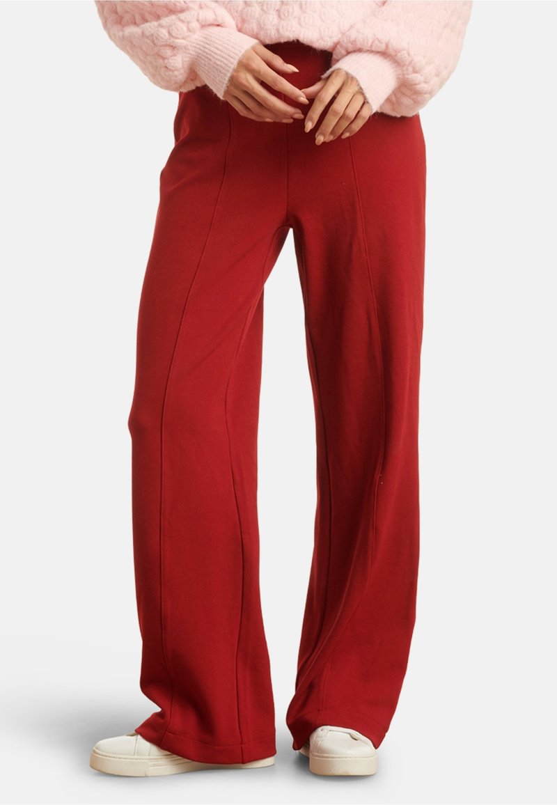 Red wide-leg pants made of soft fabric, featuring vertical seams, a comfortable waistband, and paired with white sneakers.