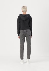 Svart hettegenser med grå denim jeans. Hettegenseren har lange ermer og en avslappet passform. Jeansene har baklommer og en avsmalnende ben.