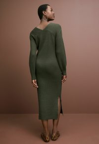 Rochie tricotată ribbed de culoare verde măslin, cu mâneci lungi, design cu decolteu în V la spate și fante laterale până la coapsă, asortată cu pantofi plate cu imprimeu de leopard.