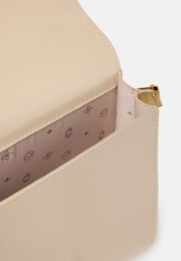 Borsa in pelle beige con una superficie liscia. All'interno presenta una fodera rosa chiaro con motivi grafici discreti e una chiusura con cerniera dorata.
