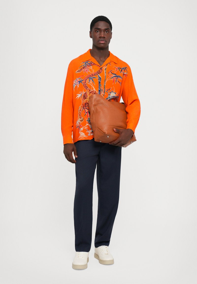Oranges Kurzarmhemd mit floralem und animalischem Print, marineblaue Hose, weiße Sneakers und eine braune Ledertasche mit strukturierter Oberfläche.