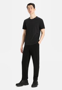 Black short-sleeve t-shirt and matching black trousers. Fabric appears smooth. Model wears sturdy black boots with laces. Simple design.